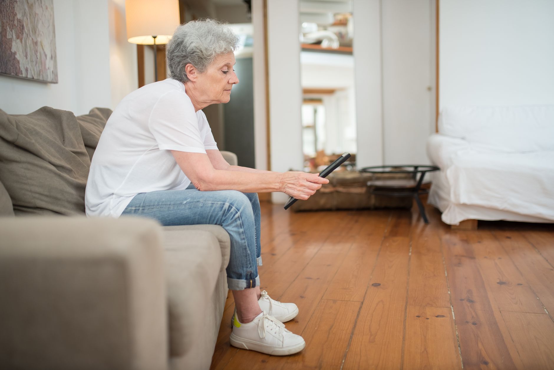 a senior woman with a tablet listening to a smart speaker in an armchair
