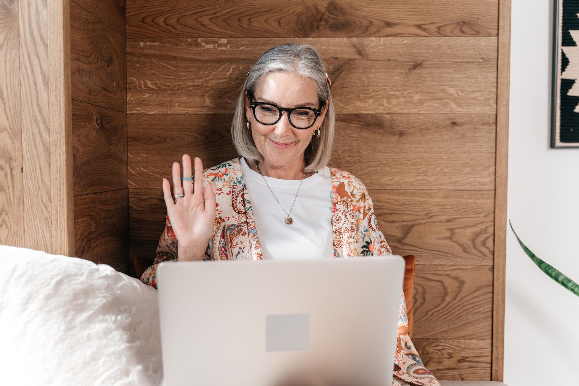a senior woman waving at a laptop screen during a family video call