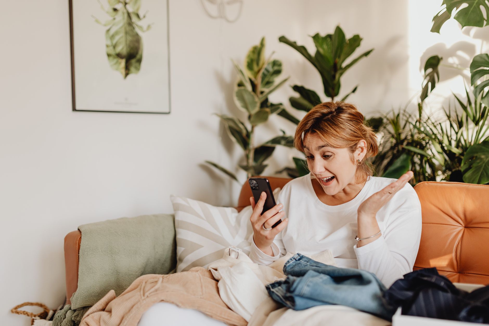 a smiling senior woman holding a smartphone and making a video call in a bright living room