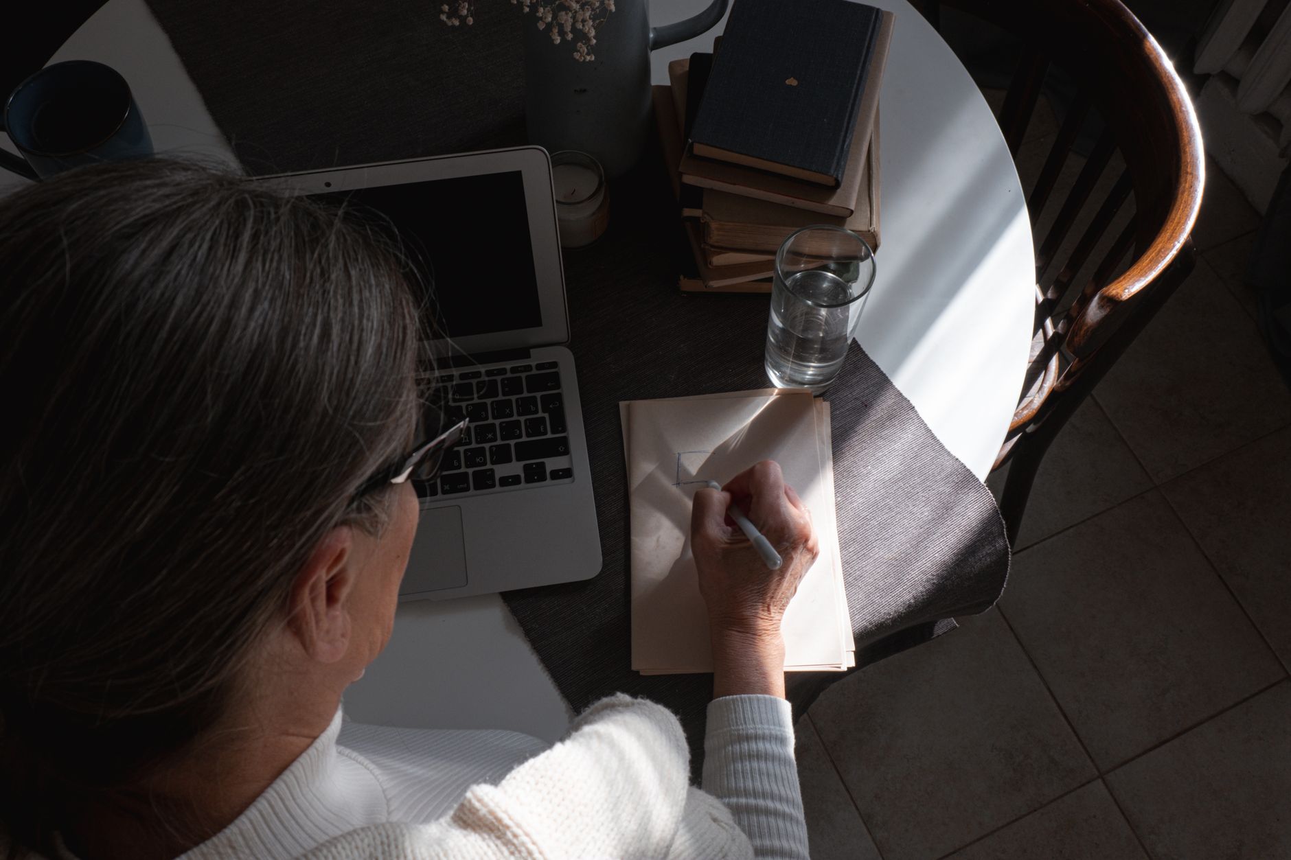 a senior woman writes a passphrase in a paper notebook next to a laptop