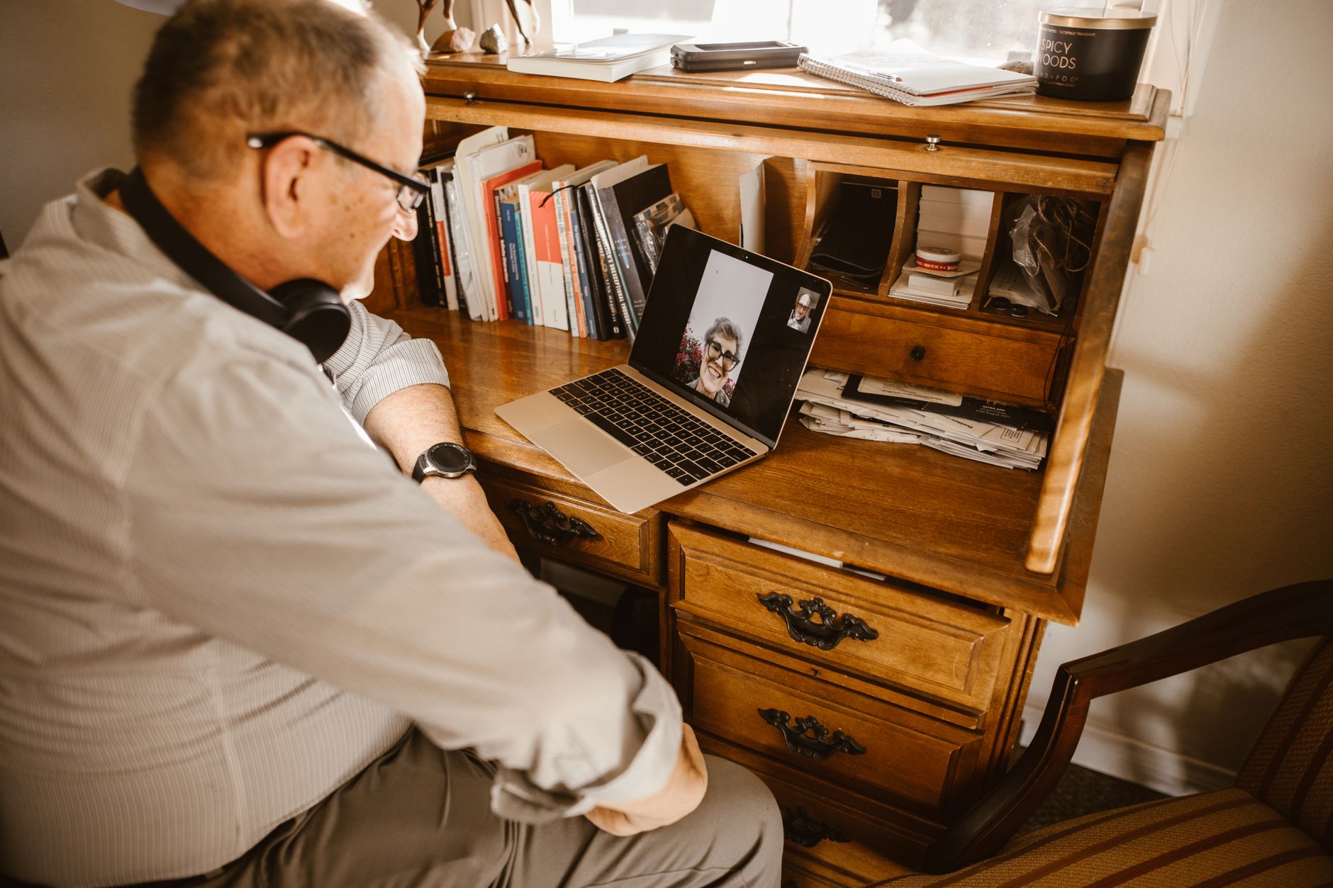 a senior woman wearing headphones while talking on a video call in her kitchen